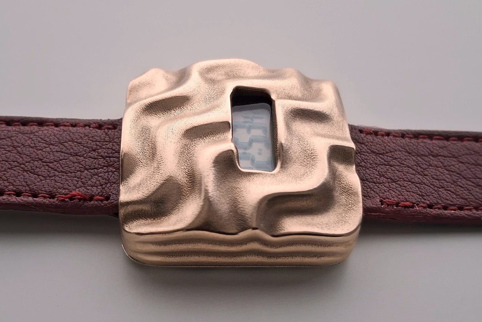 Askja from a low side angle, showing the depth of the bronze case, its layered edge and where the leather strap meets the case