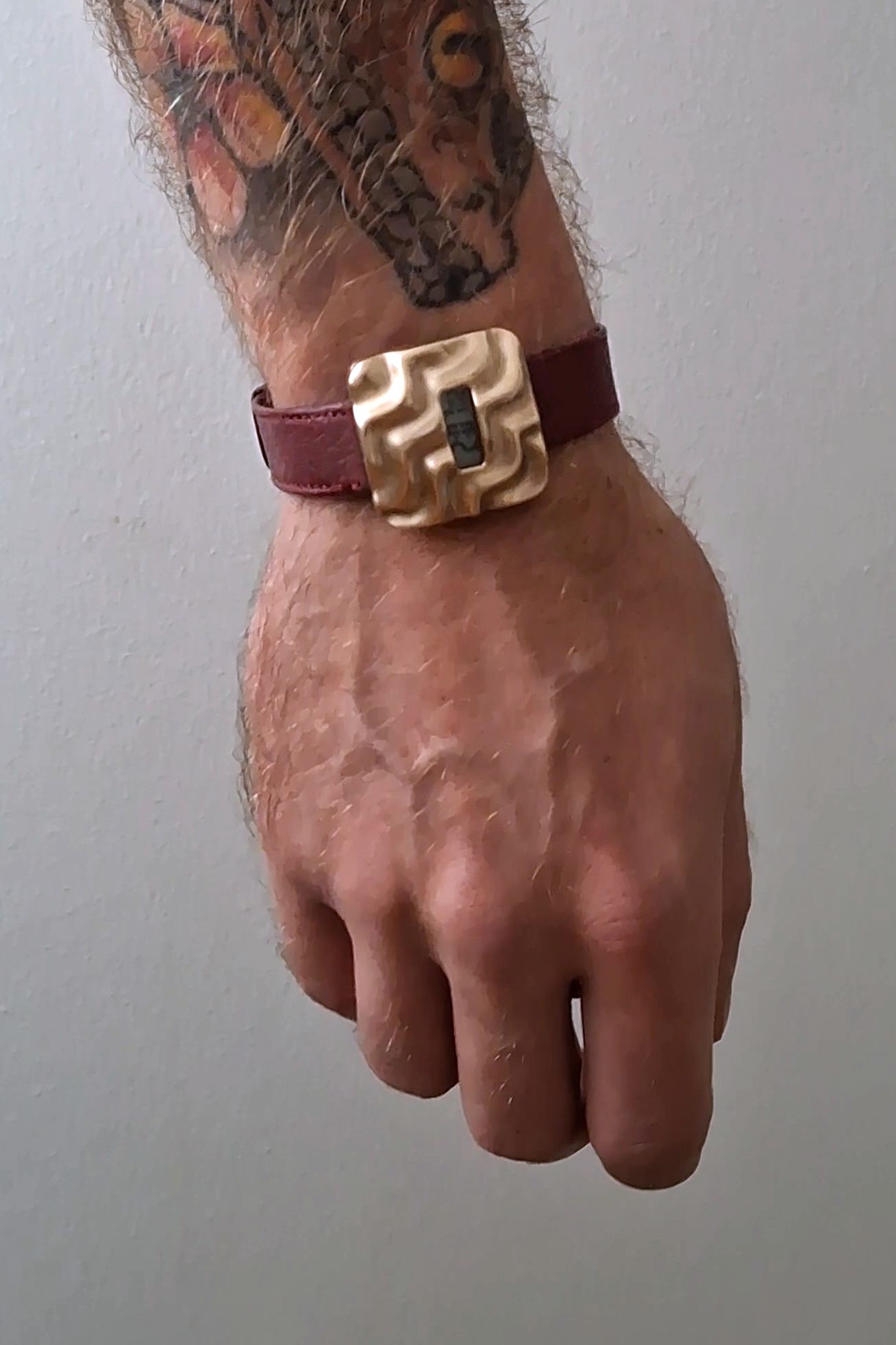 Askja worn on the wrist: the bronze case on a dark red leather strap, shown at hand scale
