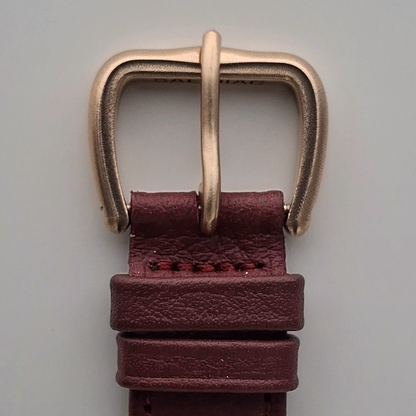 The finished bronze buckle with its tongue, fitted to the dark red leather strap